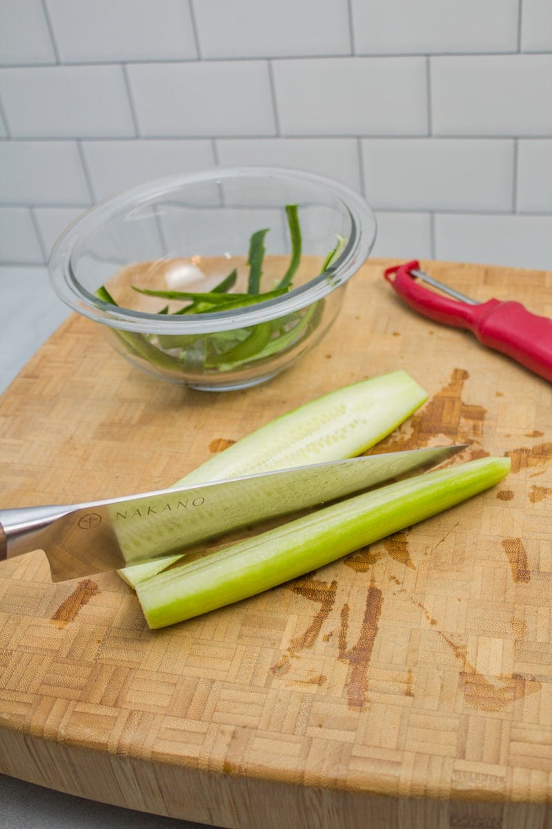 Slicing a peeled cucumber in half.