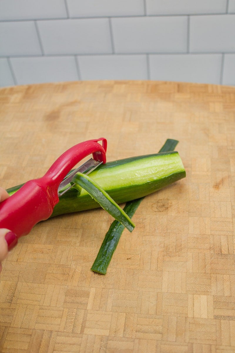 Peeling a cucumber with a vegetable peeler.
