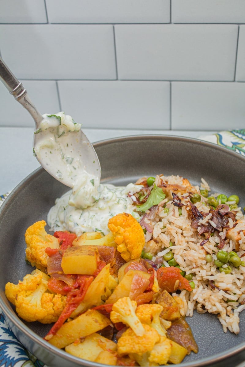 Spooning cucumber raita onto a plate of Indian food.