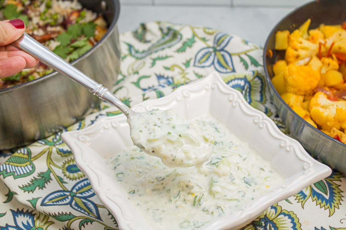 Scooping a spoonful of cucumber raita from a bowl.