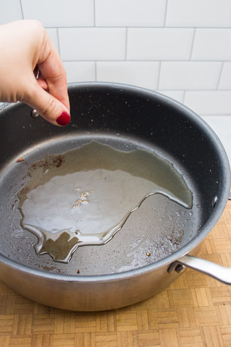 Adding cumin seeds to a skillet with hot oil.