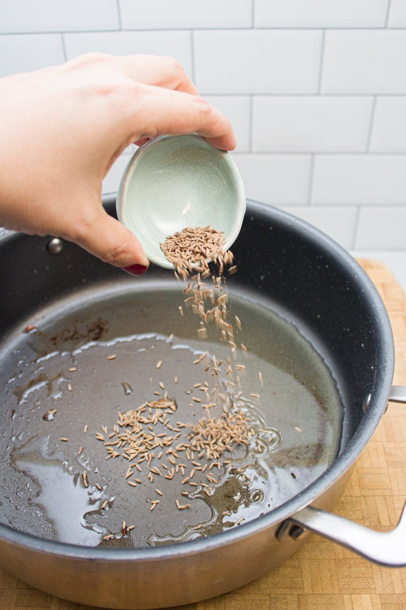 Adding cumin seeds to a skillet with hot oil.