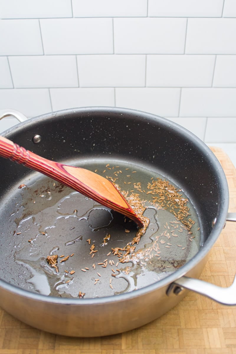Adding cumin seeds to a skillet with hot oil.
