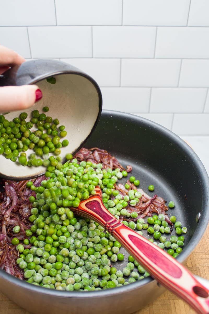 Adding peas to a skillet of caramelized onions.