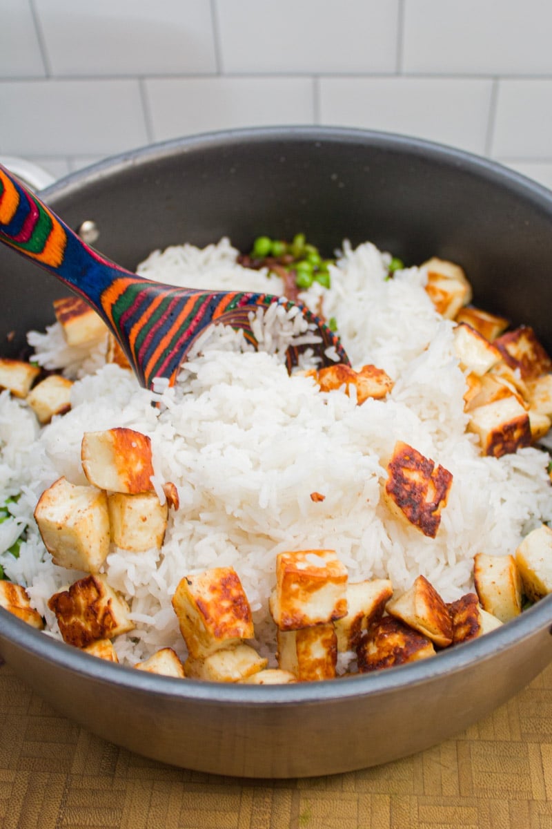 Mixing basmati rice into a skillet with paneer, peas, and caramelized onions.