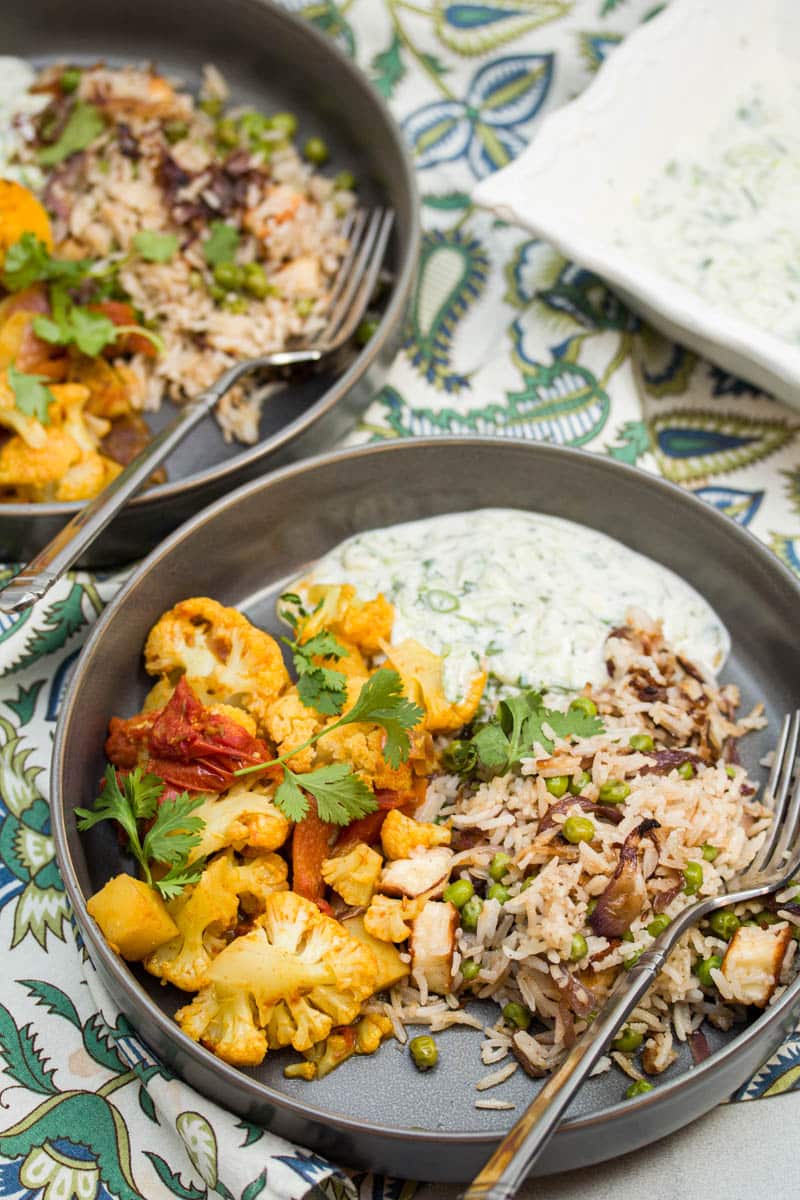 Indian pullao, aloo gobi, raita, and naan served in a dish.