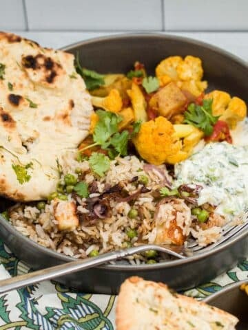 Indian pullao, aloo gobi, raita, and naan served in a dish.