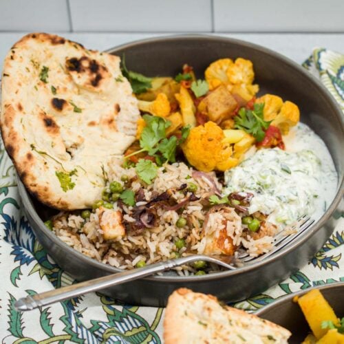 Indian pullao, aloo gobi, raita, and naan served in a dish.