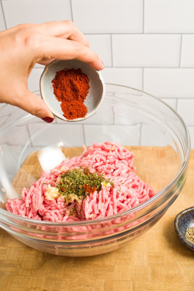 Adding ground paprika to a bowl of ground pork and spices.