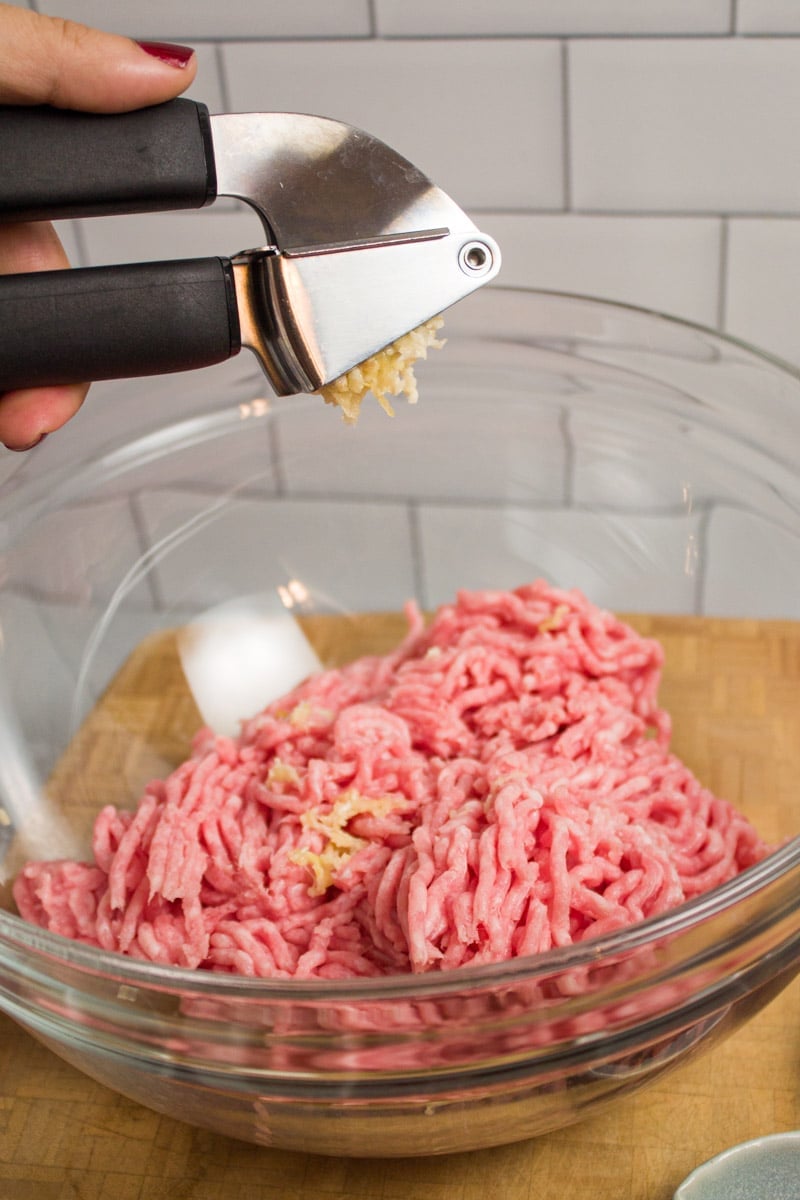 Adding minced garlic to a bowl of ground pork.