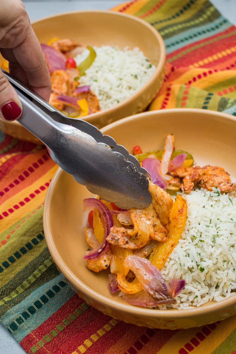 Adding chicken fajita mixture to a bowl with cilantro lime rice.
