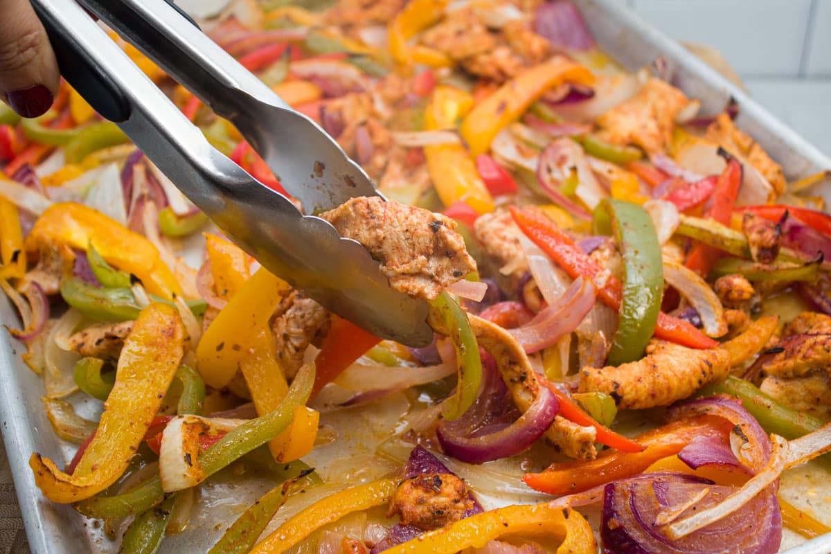 Grabbing chicken fajita mixture from a sheet pan with tongs.