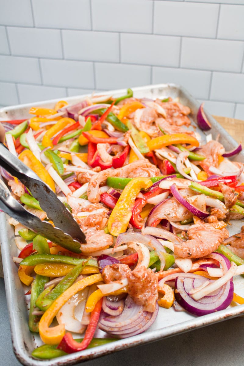Spreading out fajita marinated chicken, bell peppers, and onions on a sheet pan.
