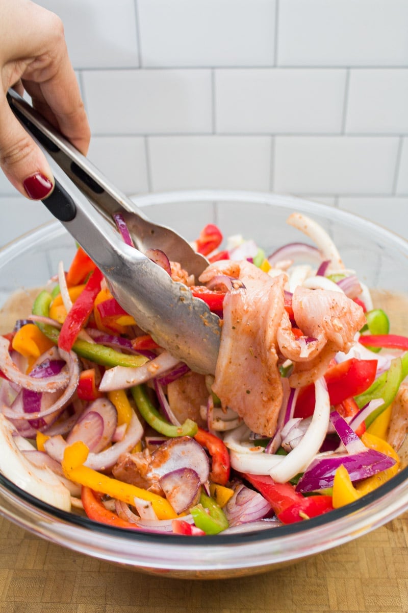 Tossing sliced onions, bell peppers, and chicken in a bowl of fajita marinade.