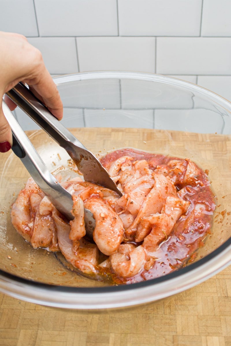 Tossing sliced chicken in a bowl of fajita marinade with tongs.