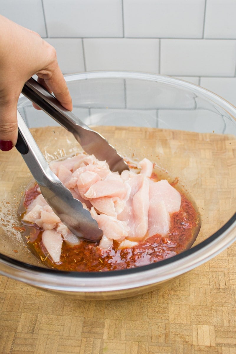 Tossing sliced chicken in a bowl of fajita marinade with tongs.