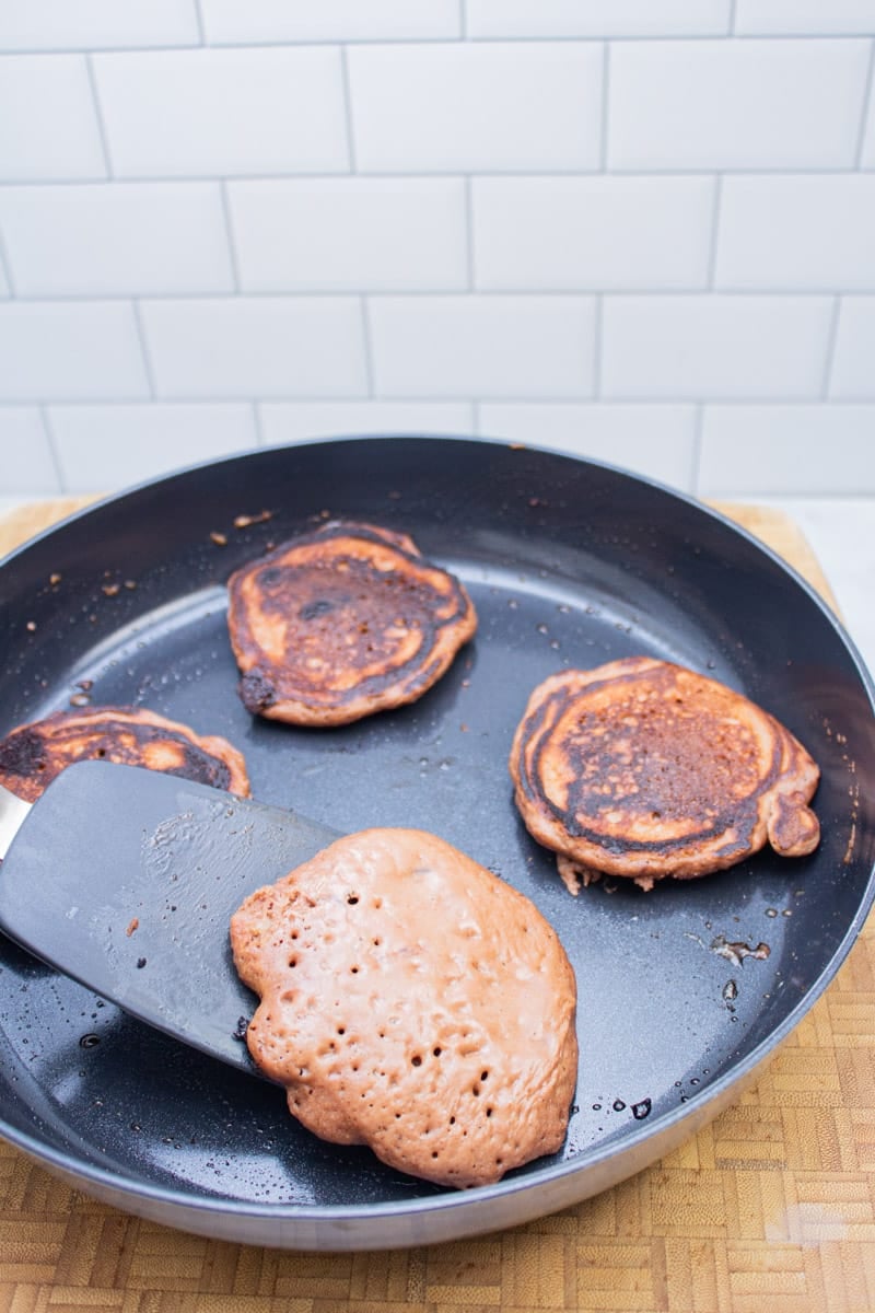 Flipping chocolate chocolate chip pancakes with a spatula in a nonstick skillet.