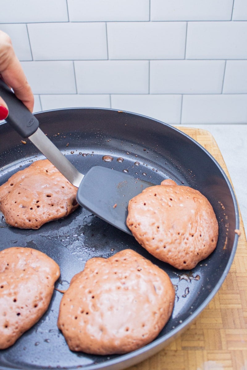 Flipping chocolate chocolate chip pancakes with a spatula in a nonstick skillet.