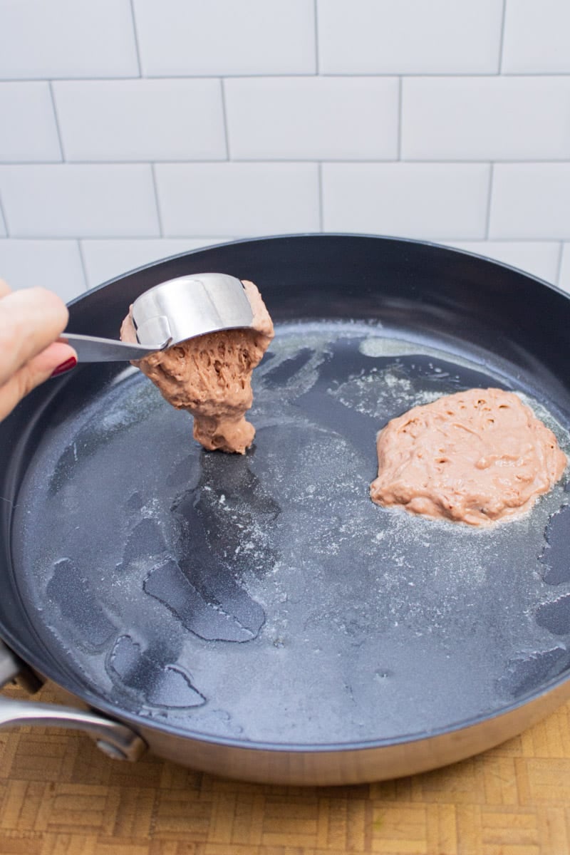 Adding portions of chocolate chocolate chip pancake batter into a skillet to cook.
