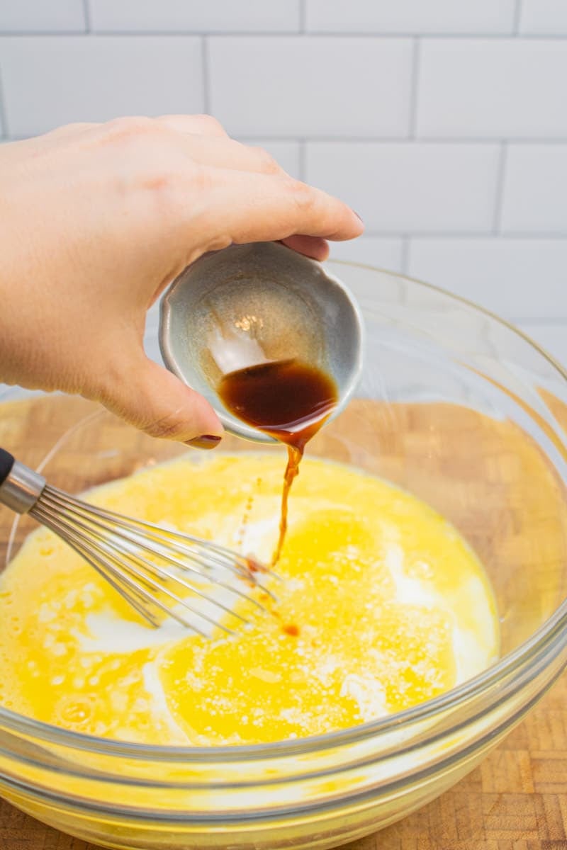 Adding vanilla extract to a mixing bowl of wet ingredients for chocolate chocolate chip pancakes.