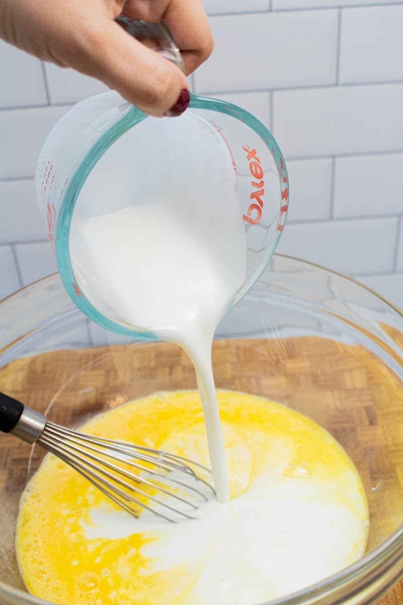 Adding buttermilk to a mixing bowl of whisked eggs.