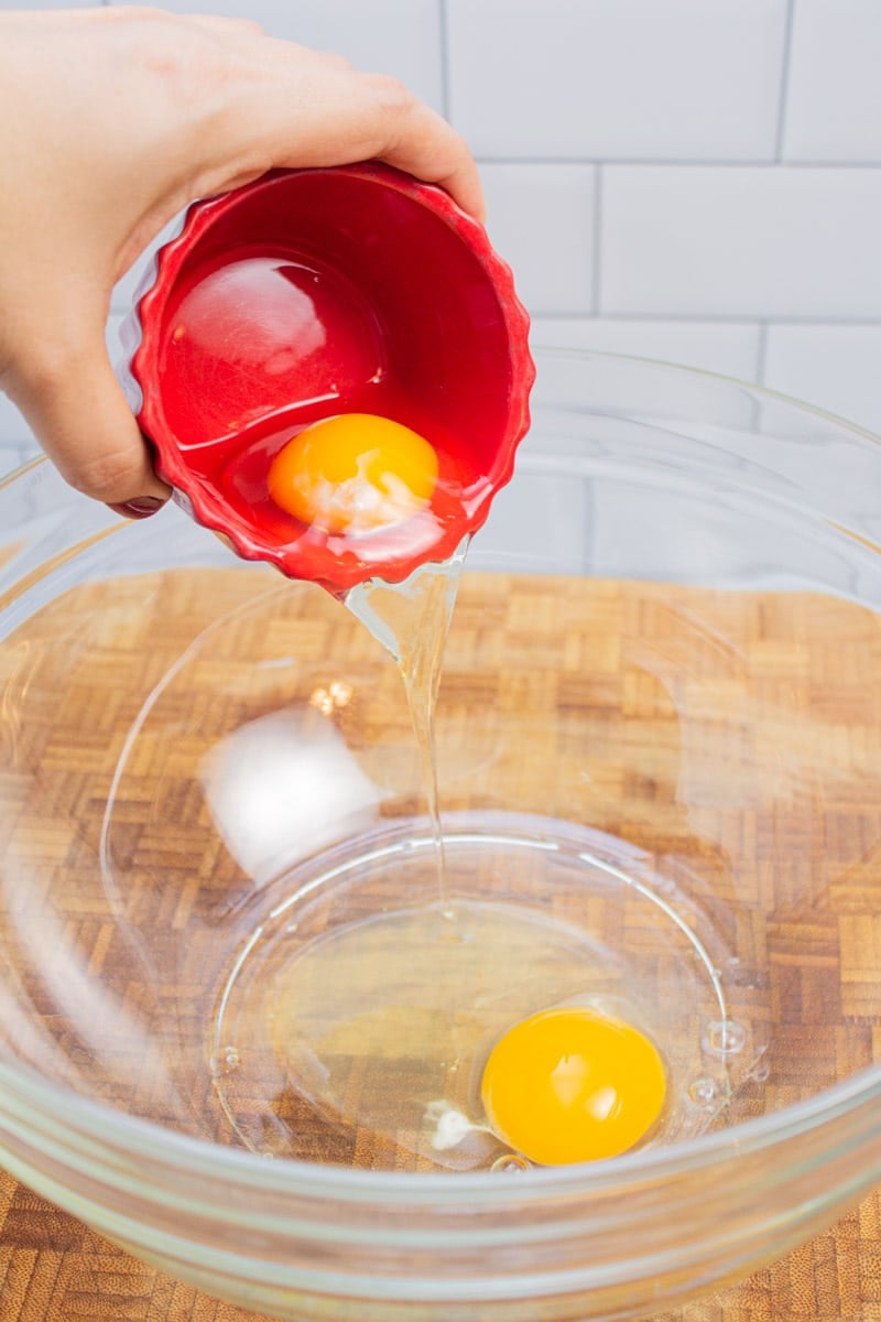 Adding eggs to a mixing bowl.