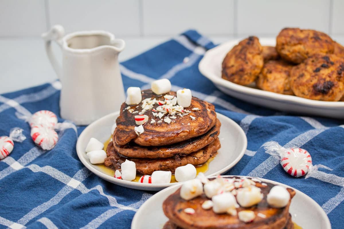 Plates of chocolate chocolate chip pancakes with peppermints, mini marshmallows, and maple syrup.