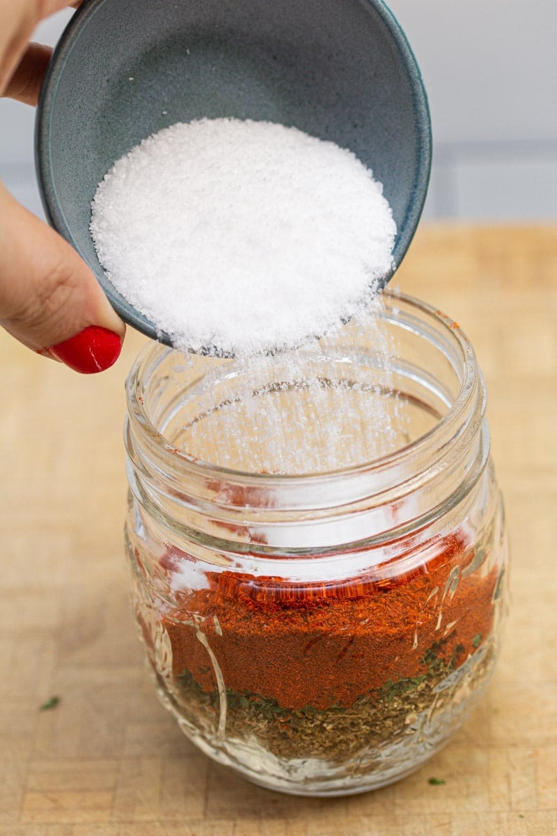 Adding kosher salt to a jar to make a breakfast sausage seasoning blend.