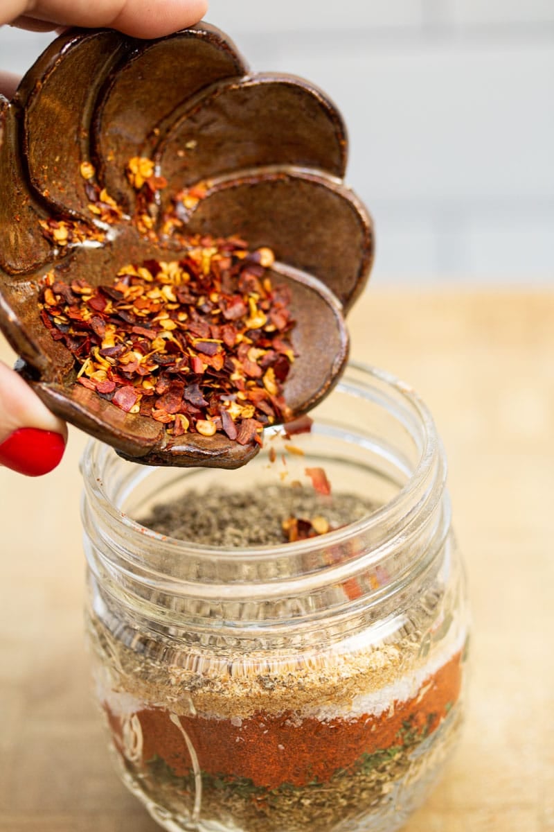 Adding red pepper flakes to a jar to make a breakfast sausage seasoning blend.