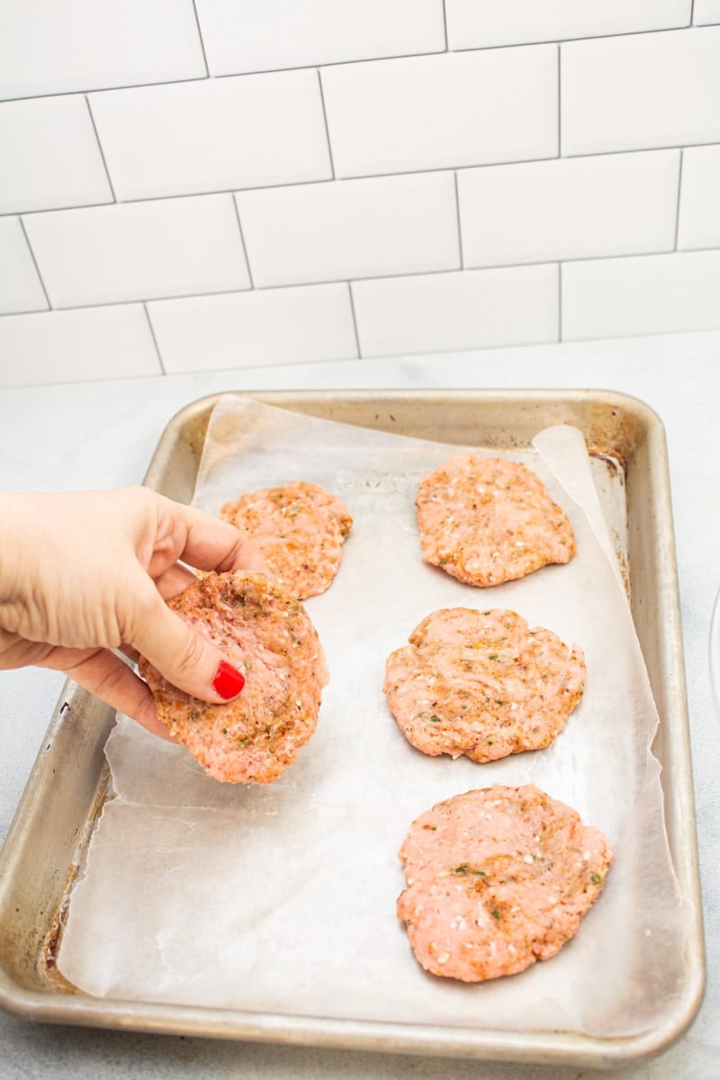 Adding raw turkey sausage patties to a baking sheet lined with wax paper.