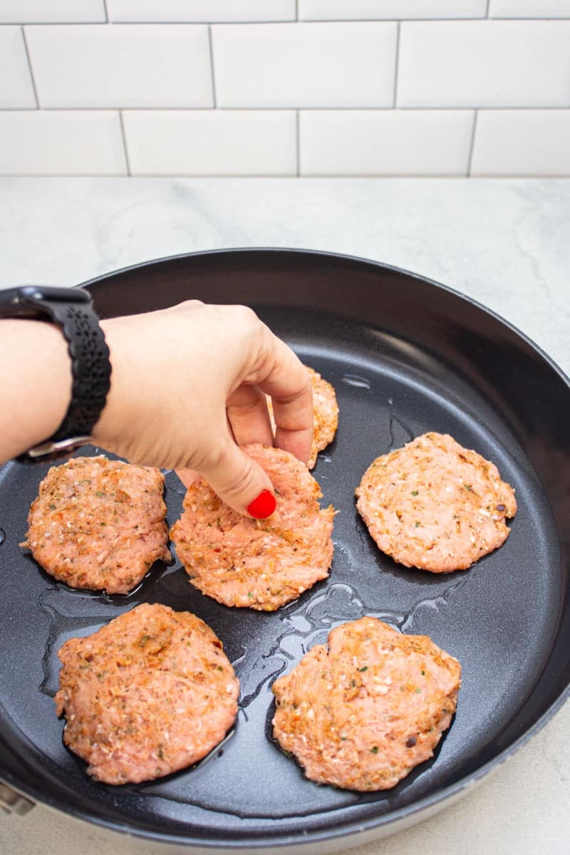 Placing turkey sausage patties in a skillet.