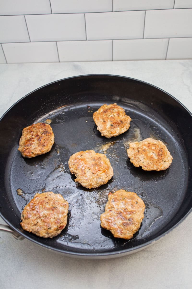 Turkey sausage patties frying in a skillet.
