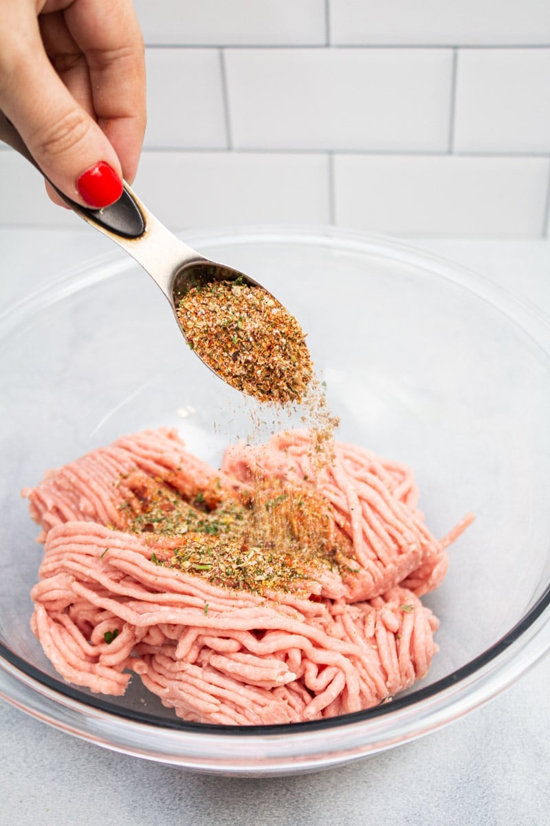 Adding a breakfast sausage spice blend to a bowl of ground turkey.