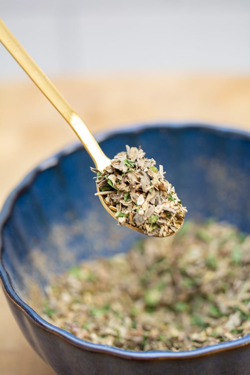 Scooping a spoonful of a homemade Italian seasoning blend from a bowl.