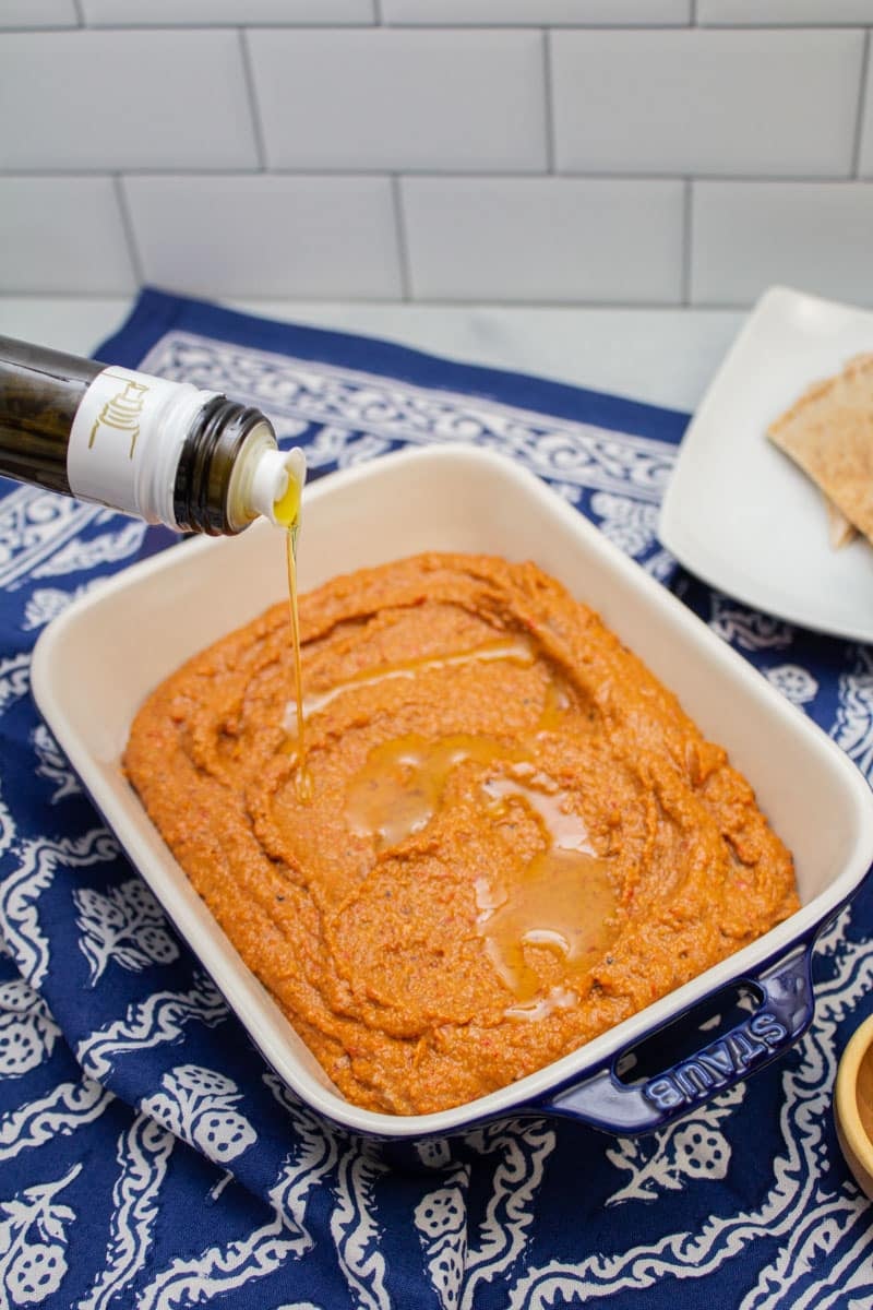 Drizzling olive oil over the top of a serving dish of muhammara.