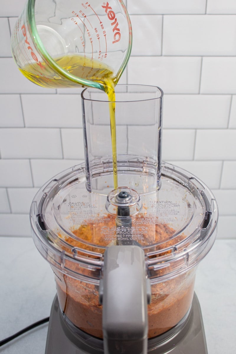Drizzling olive oil into a food processor of muhammara.