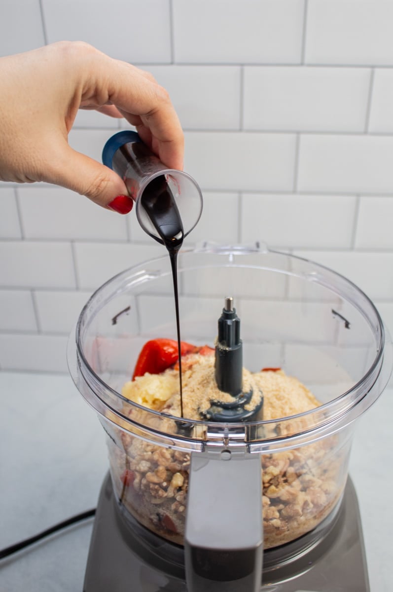 Adding pomegranate molasses to a food processor with ingredients to make muhammara.