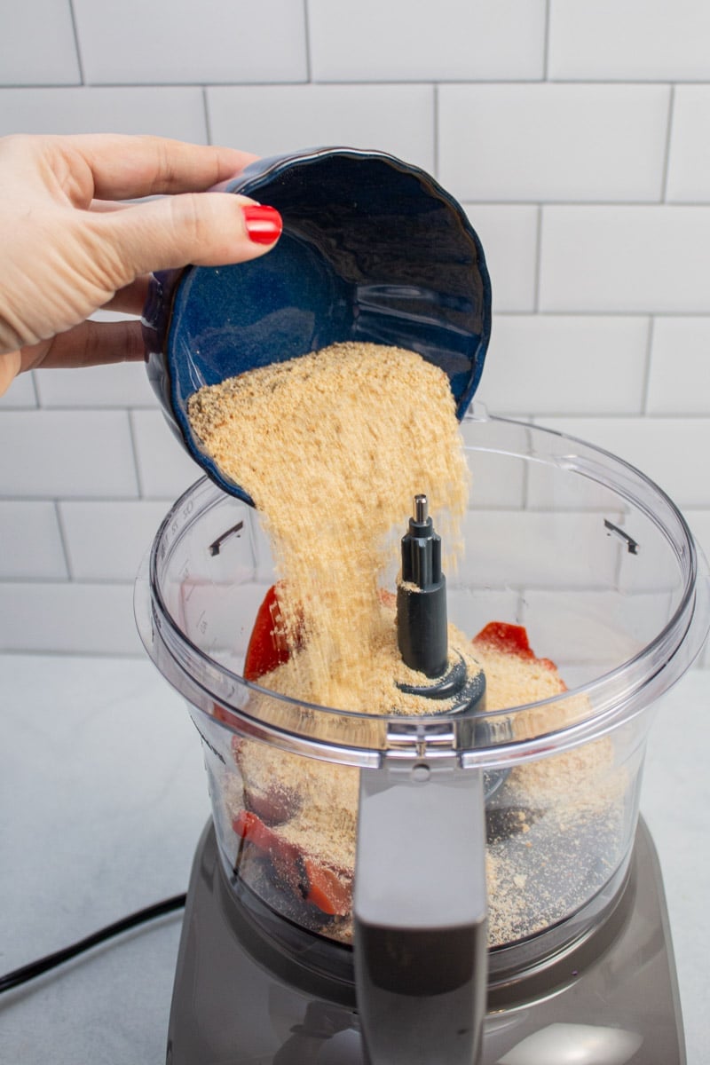 Adding breadcrumbs to a food processor with roasted red peppers.