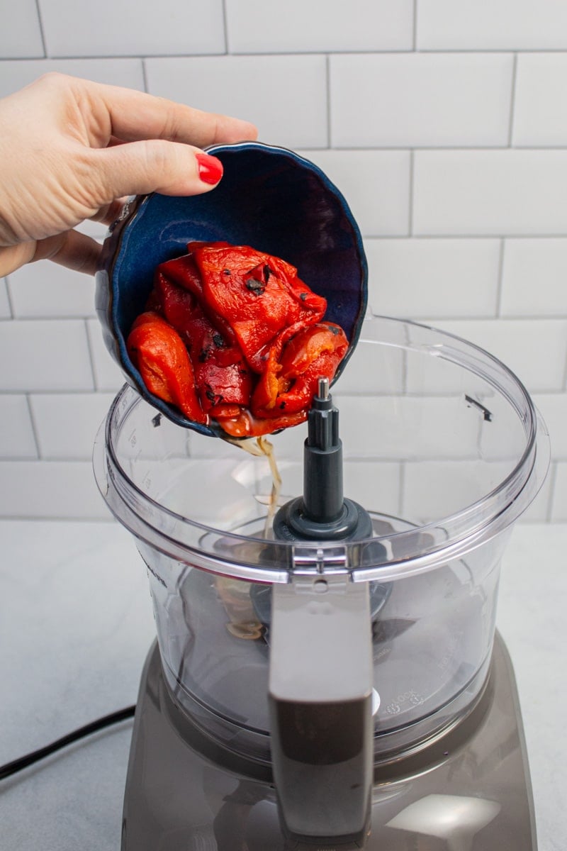 Adding roasted red peppers to a food processor to make muhammara.