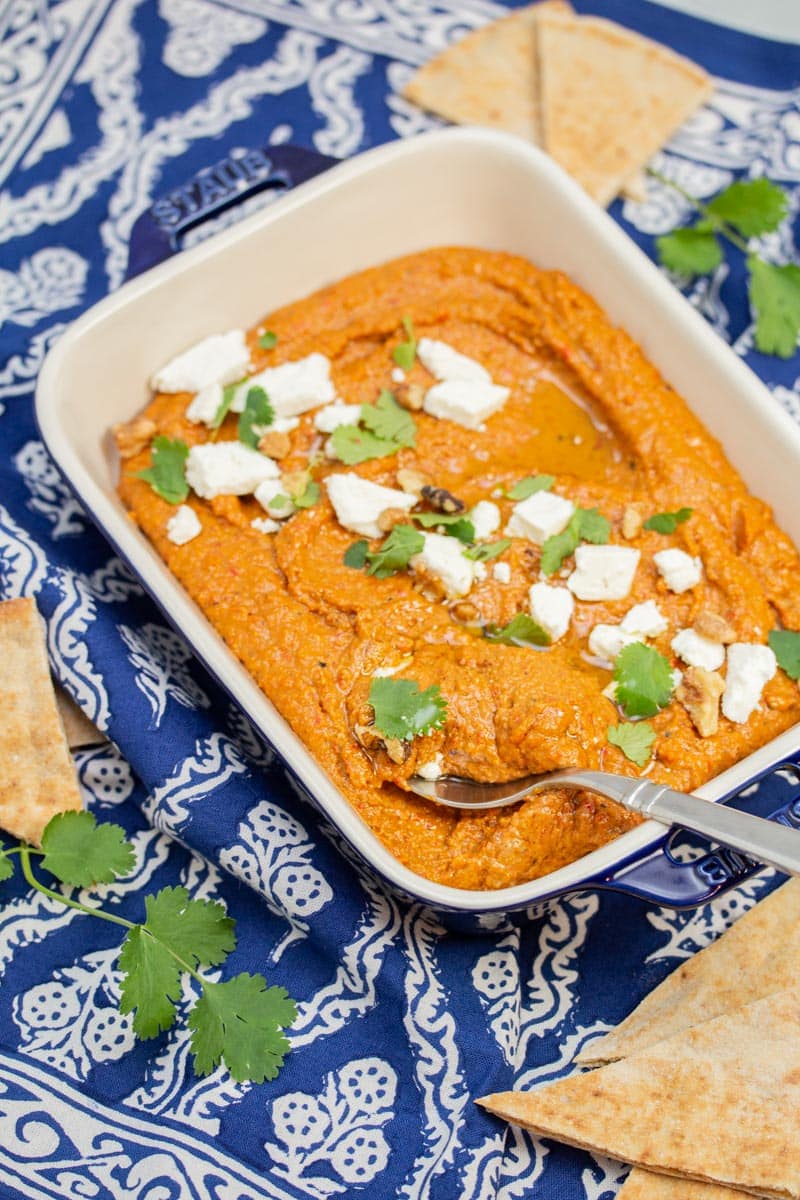 Muhammara garnished with feta cheese, cilantro, and walnuts with pita bread alongside.