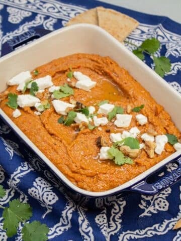 Muhammara garnished with feta cheese, cilantro, and walnuts with pita bread alongside.