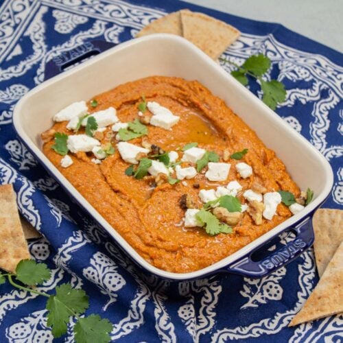Muhammara garnished with feta cheese, cilantro, and walnuts with pita bread alongside.