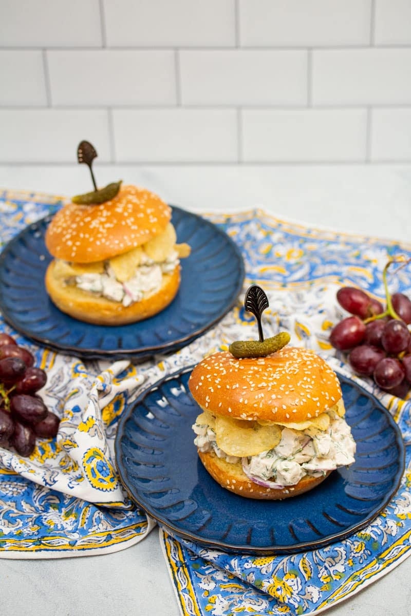 Dill chicken salad sandwiches with potato chips on plates.