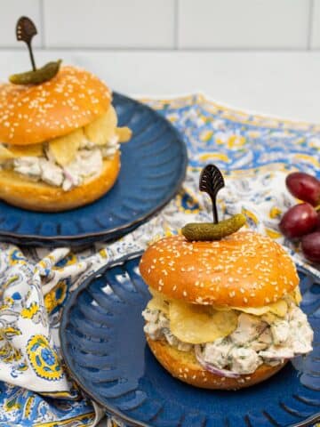 Dill chicken salad sandwiches with potato chips on plates.
