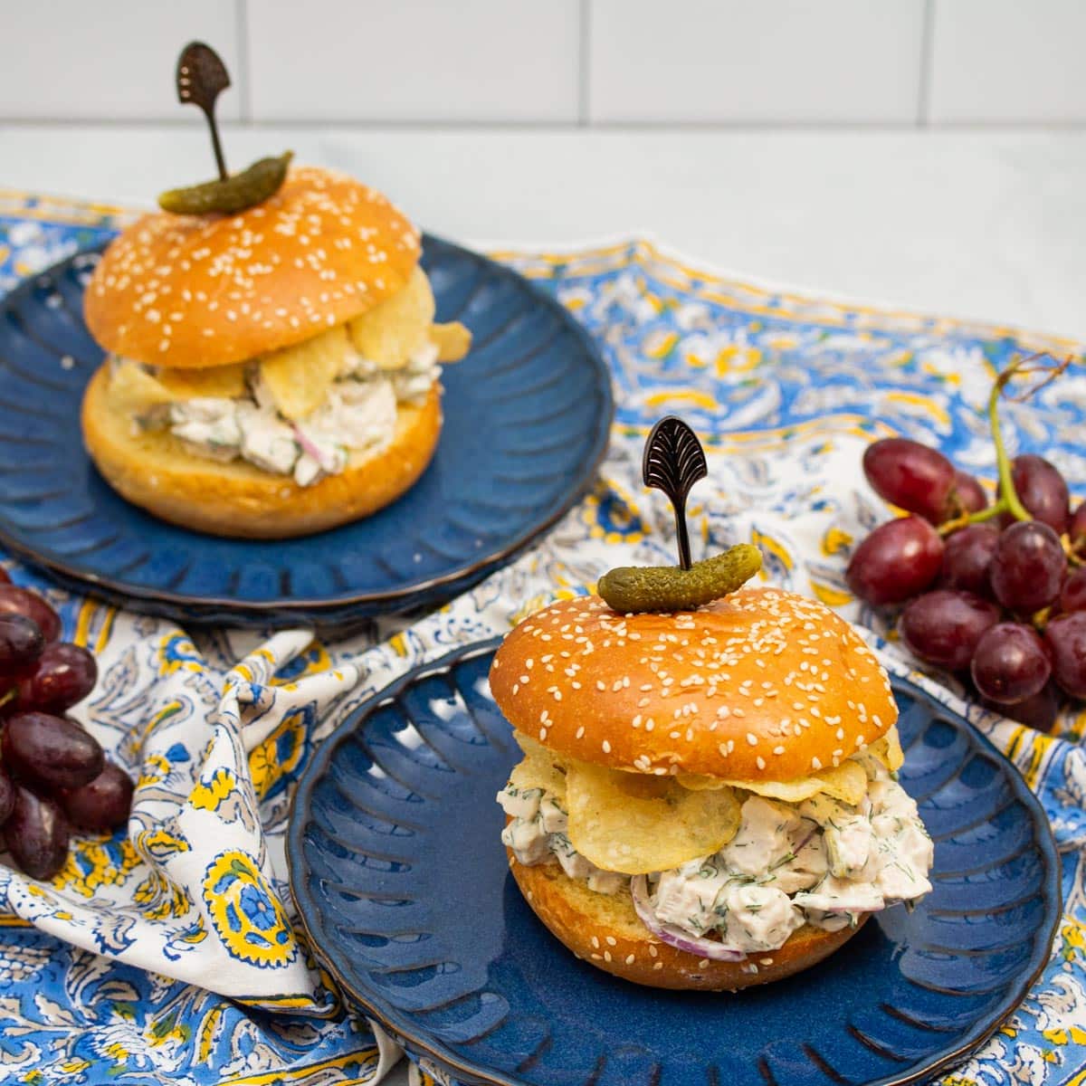 Dill chicken salad sandwiches with potato chips on plates.