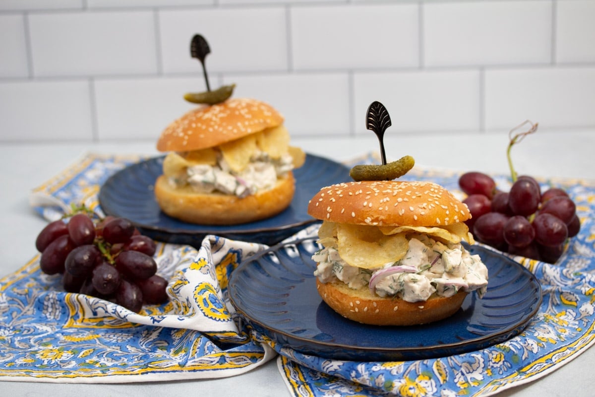 Dill chicken salad sandwiches with potato chips on plates.
