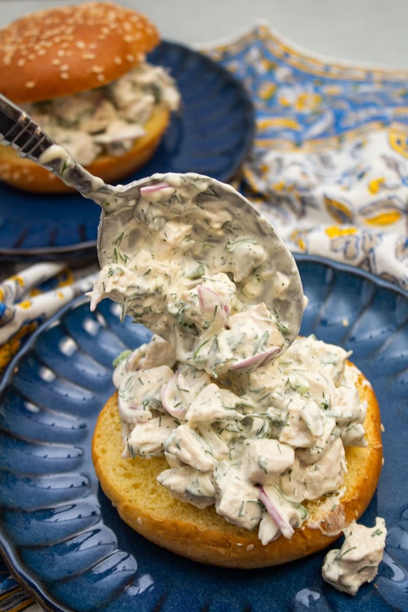 Scooping dill chicken salad onto a sandwich roll.