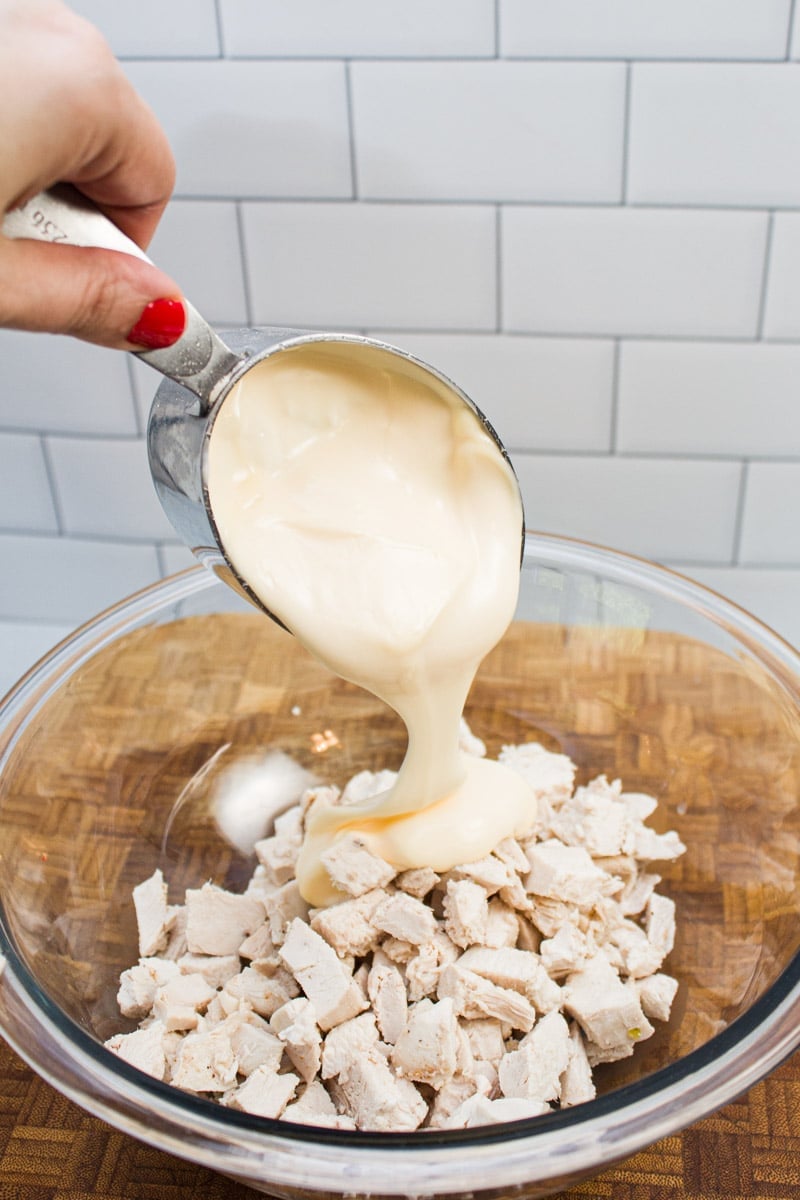 Adding mayonnaise and Greek yogurt to a bowl of chopped, cooked chicken.